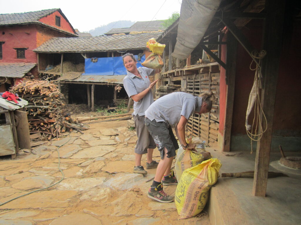 Two travelers help carry sacks in the courtyard of a traditional village home in Aathrai, eastern Nepal.